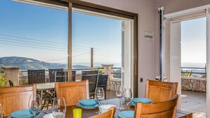 A dining area with a table set for four, large windows offering a view of a mountainous landscape, and a stone wall. - Beautiful home in Sant Cebrià de Vallalt (Sant Cebrià de Vallalt)