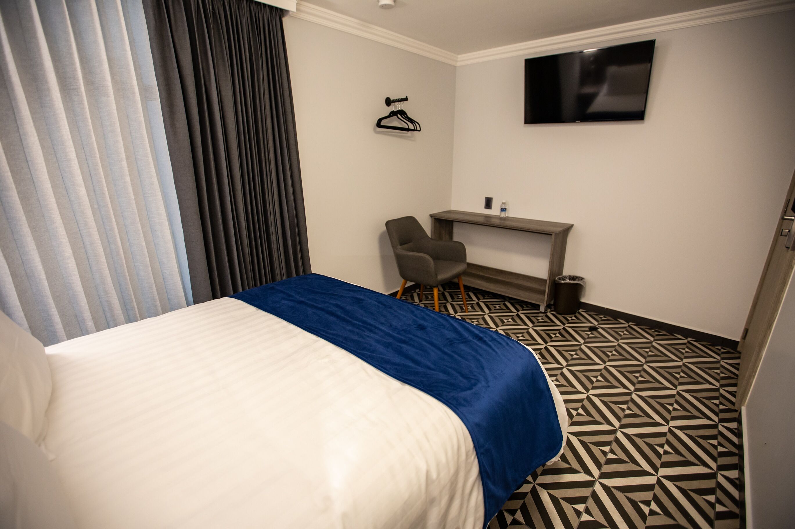 Una habitación de hotel con cama, escritorio, silla, televisor y piso con diseño.
