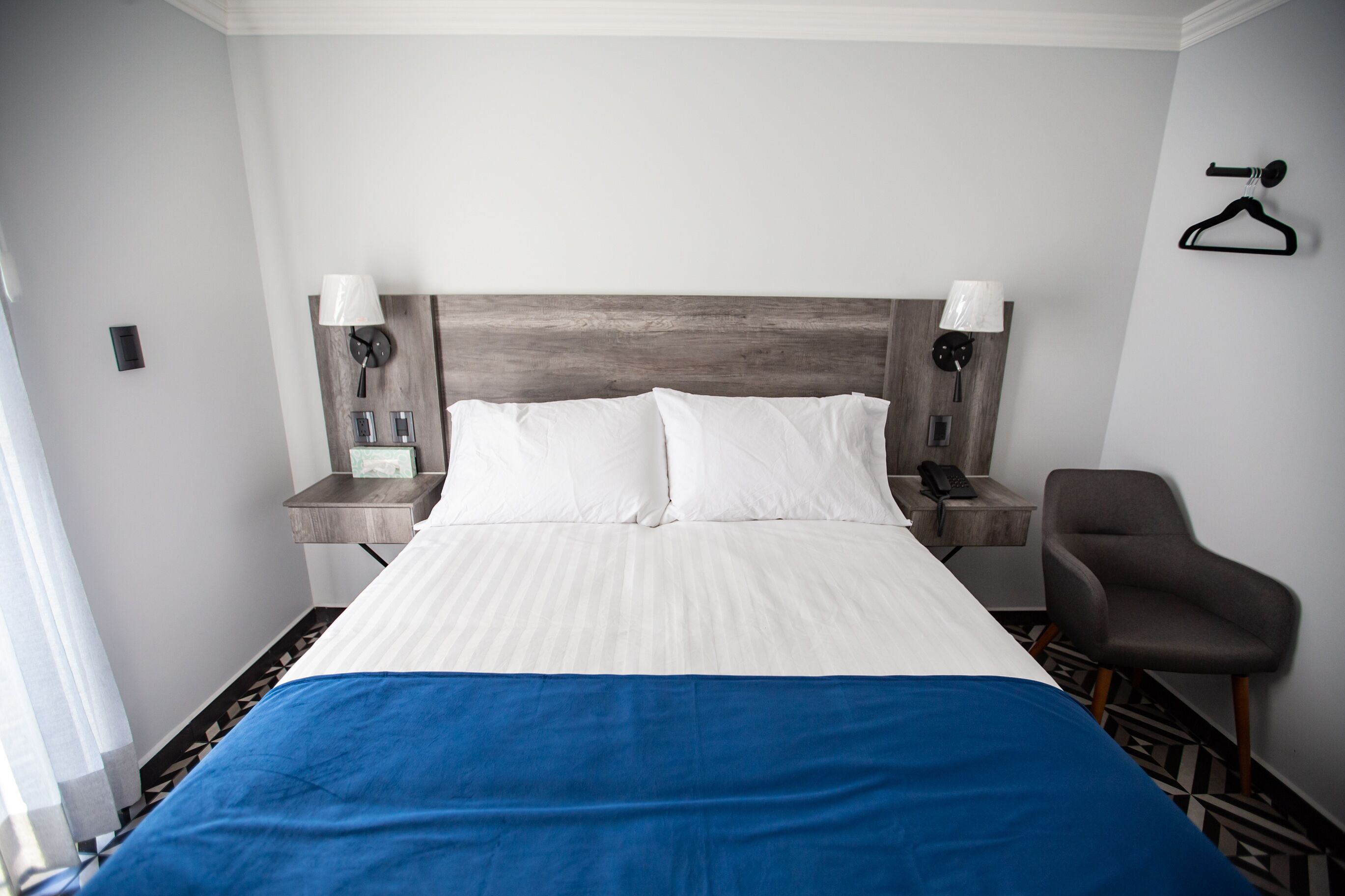 A hotel room with a large bed, two bedside tables with lamps, a chair, and a coat hanger on the wall.