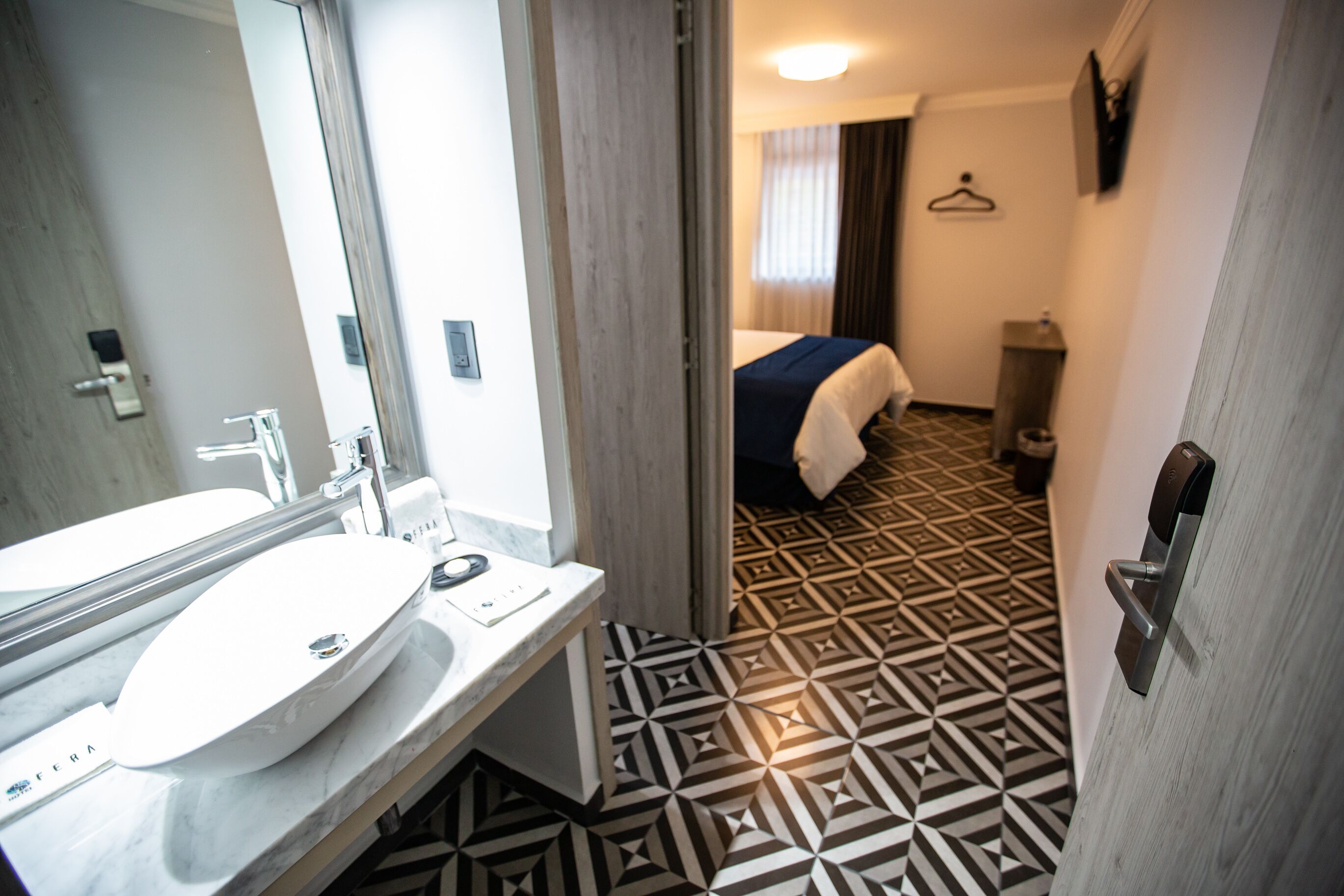 A hotel bathroom with a large mirror, a sink, and a patterned floor.