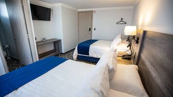 Habitación de hotel con dos camas, televisor montado en la pared, mesita de noche con lámpara y una puerta con el letrero de prohibido fumar.