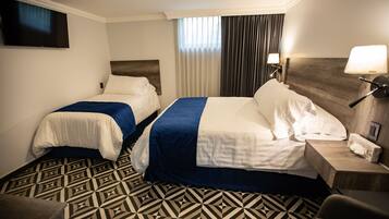 Una habitación de hotel con dos camas, televisión, escritorio y suelo estampado.