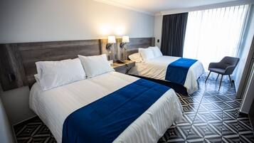 A hotel room with two beds, a nightstand with a phone and lamps, a chair, and a patterned floor.