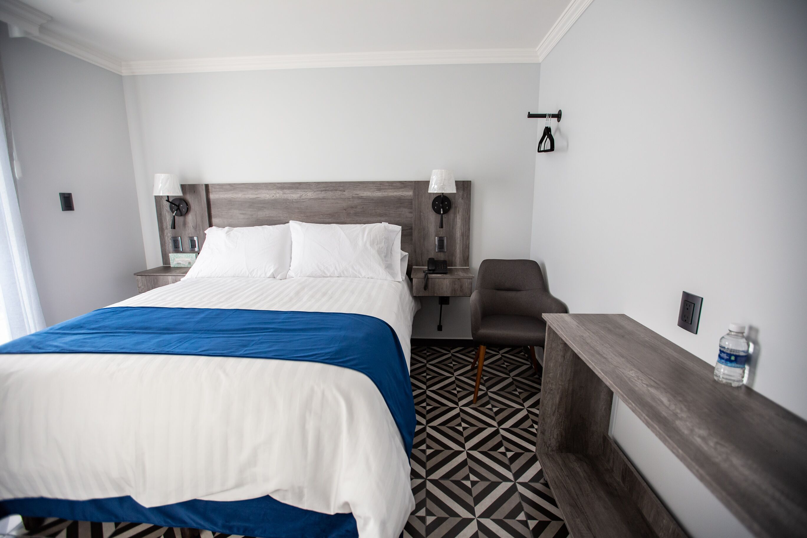 Ein Hotelzimmer mit einem großen Bett, zwei Nachttischen mit Lampen, einem Sessel und einem kleinen Schreibtisch.