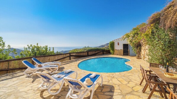 A stone pool with lounge chairs and a table, surrounded by a stone wall and vegetation. - Finca Hornillo Cómpeta by Ruralidays (Málaga)
