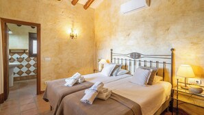 A hotel room with two beds, a bathroom with a tiled floor, and a wall-mounted air conditioner. - Finca Hornillo Cómpeta by Ruralidays (Málaga)