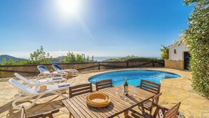 A poolside area with lounge chairs, a table with wine glasses, and a view of the sea. - Finca Hornillo Cómpeta by Ruralidays (Málaga)