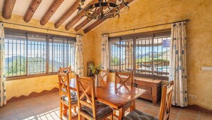 A dining area with a wooden table and chairs, large windows with metal bars, and a view of the outdoors. - Finca Hornillo Cómpeta by Ruralidays (Málaga)