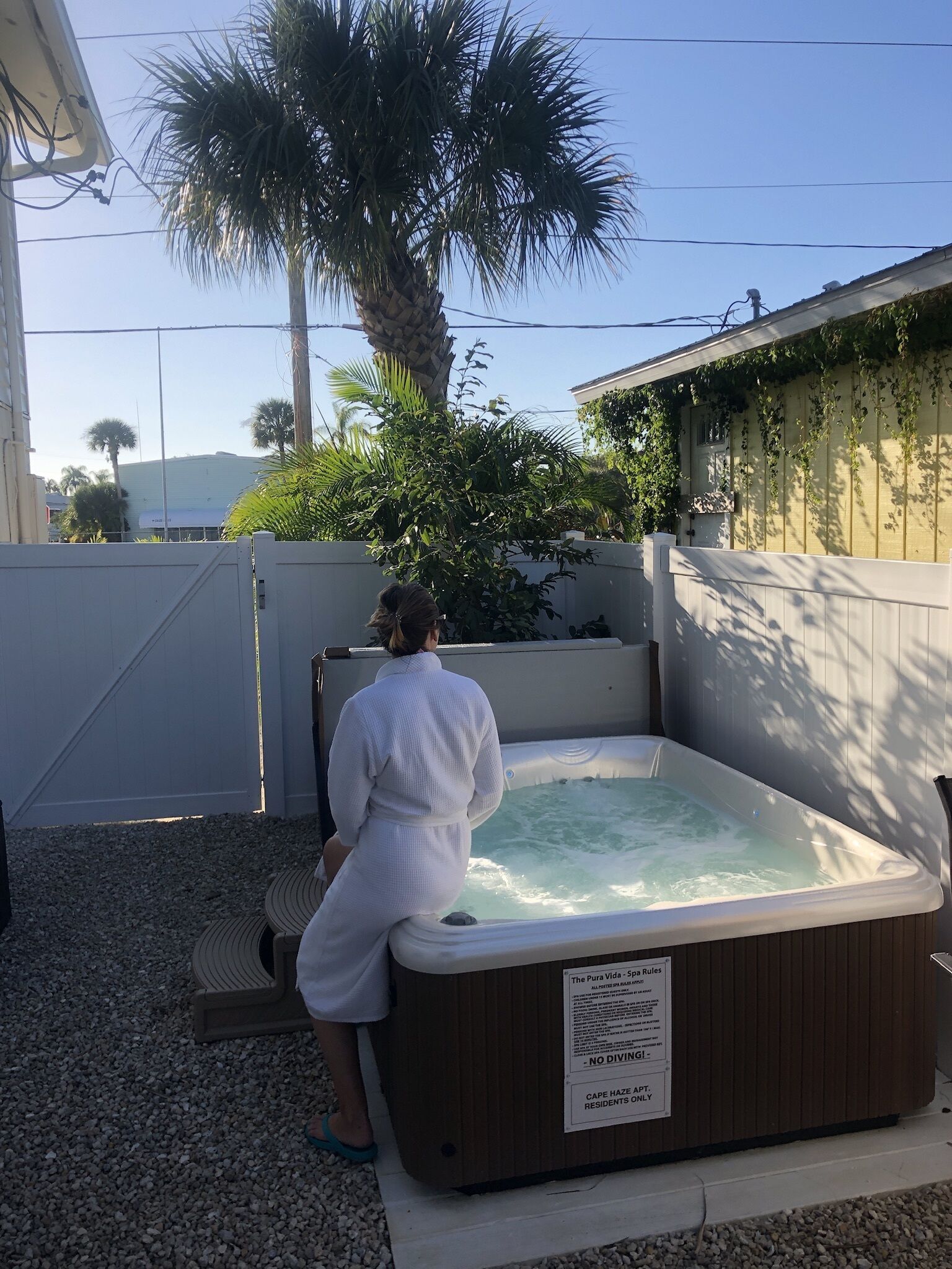 A person in a white bathrobe standing by a hot tub with a wooden exterior and a sign indicating it is for residents only.
