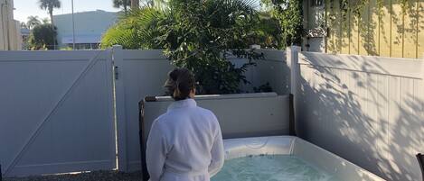 A person in a white bathrobe standing by a hot tub with a wooden exterior and a sign indicating it is for residents only.