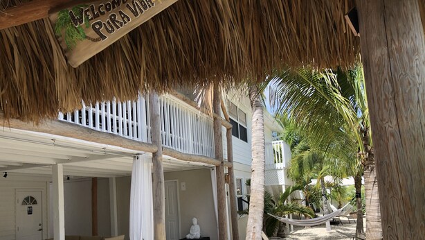 Un resort con techo de paja, balcón blanco y una hamaca.