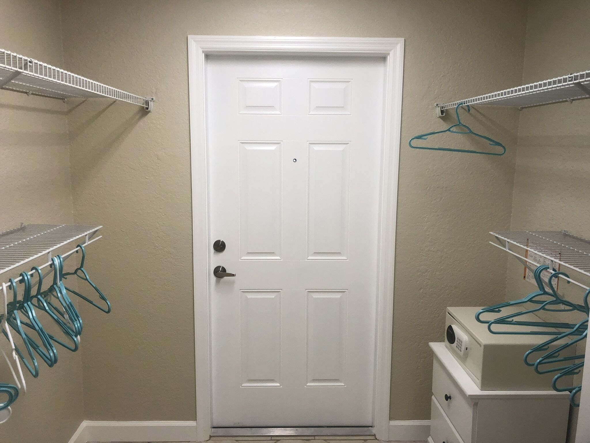 A room with a white door, beige walls, and metal shelving units on either side.