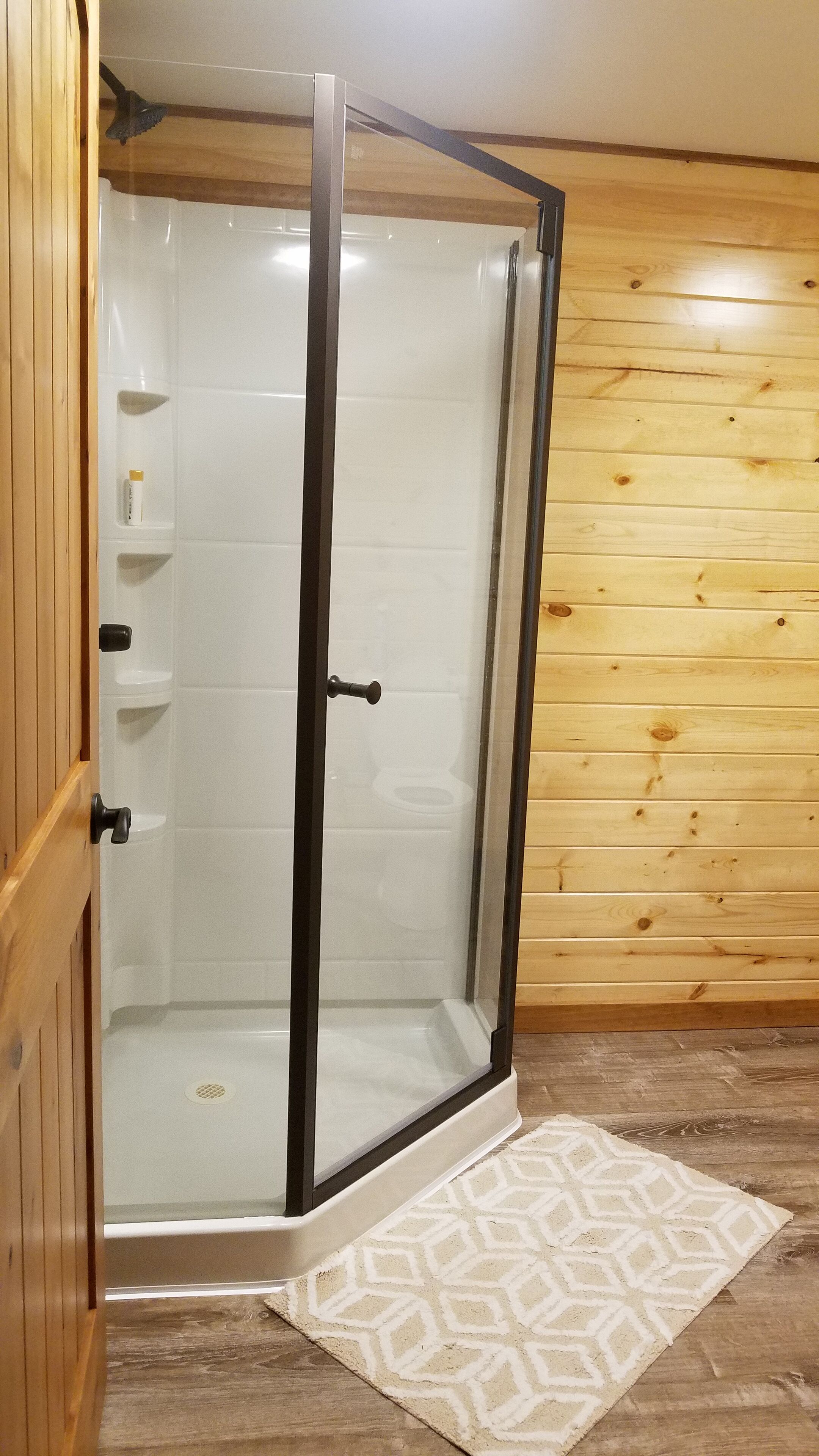 Een douche met glazen wanden, een houten inrichting, een witte betegelde vloer en een kamerbreed tapijt met patroon.
