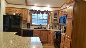 A kitchen with wooden cabinets, a black refrigerator, a coffee maker, and a window with blinds. - New on market.  Cabin with 3 beds and 3 baths surrounded by forest (Grand Marsh)