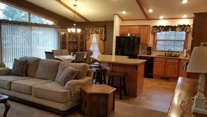 A cozy living room with a sofa and a coffee table, a dining area with a table and chairs, and a kitchen with wooden cabinets and a refrigerator. - New on market.  Cabin with 3 beds and 3 baths surrounded by forest (Grand Marsh)