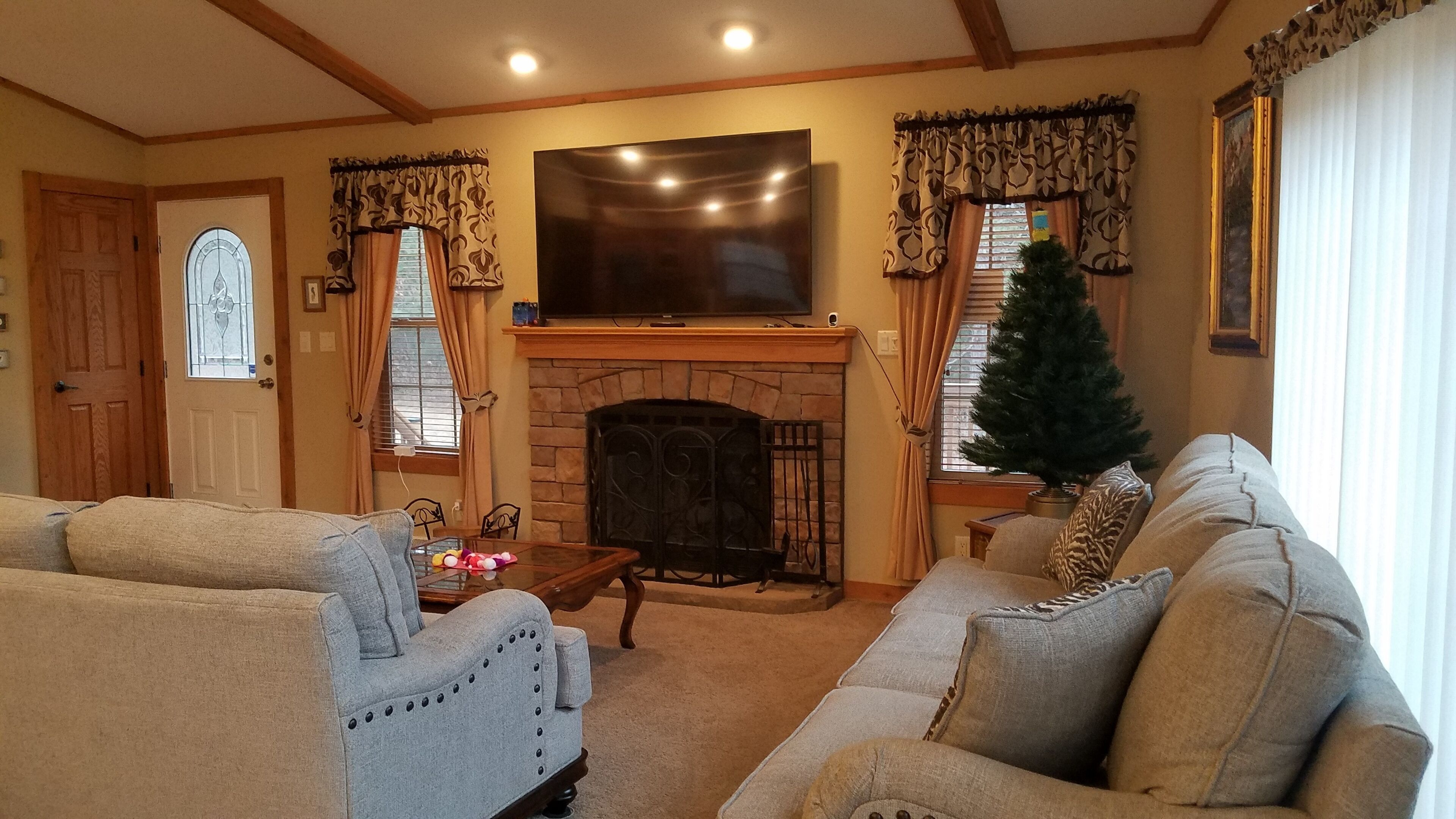 Una sala de estar con chimenea, dos sofás, un televisor y un árbol de Navidad.