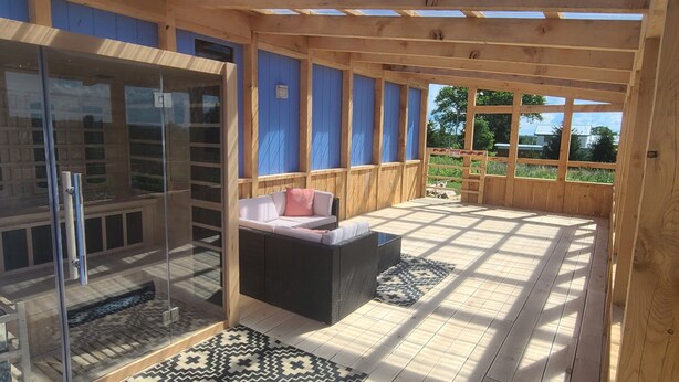 Un espacio al aire libre cubierto con una sauna de vidrio, una zona de estar con cojines y un suelo estampado.