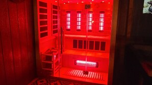 Una habitación con sauna iluminada en rojo, alfombra estampada y un reloj en la pared.