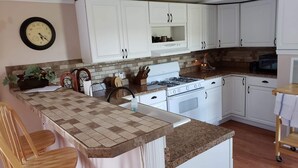 Una cocina con armarios blancos, estufa a gas, microondas y un reloj en la pared.
