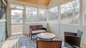 A covered patio with a wooden ceiling, large windows, a bench, and wicker furniture.