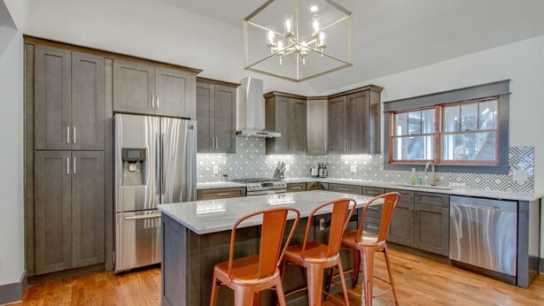 A modern kitchen with grey cabinets, stainless steel appliances, and a central island with bar stools.