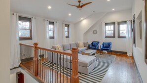 A spacious living room with a high ceiling, a wooden staircase, and a ceiling fan.