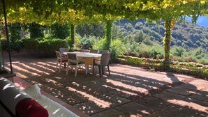An outdoor patio with a table and chairs, surrounded by lush greenery and a mountainous backdrop. - Villa with panoramic veranda 'Il Riccio' (MONTE ARGENTARIO)