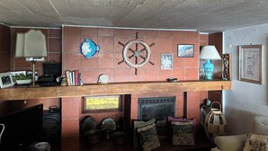 A cozy living room with a fireplace, a wooden ceiling, and various decorative items including a ship's wheel and framed pictures. - Villa with panoramic veranda 'Il Riccio' (MONTE ARGENTARIO)
