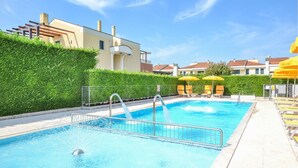 Una piscina con ringhiera metallica di sicurezza, circondata da un siepe e da una fila di ombrelloni gialli.