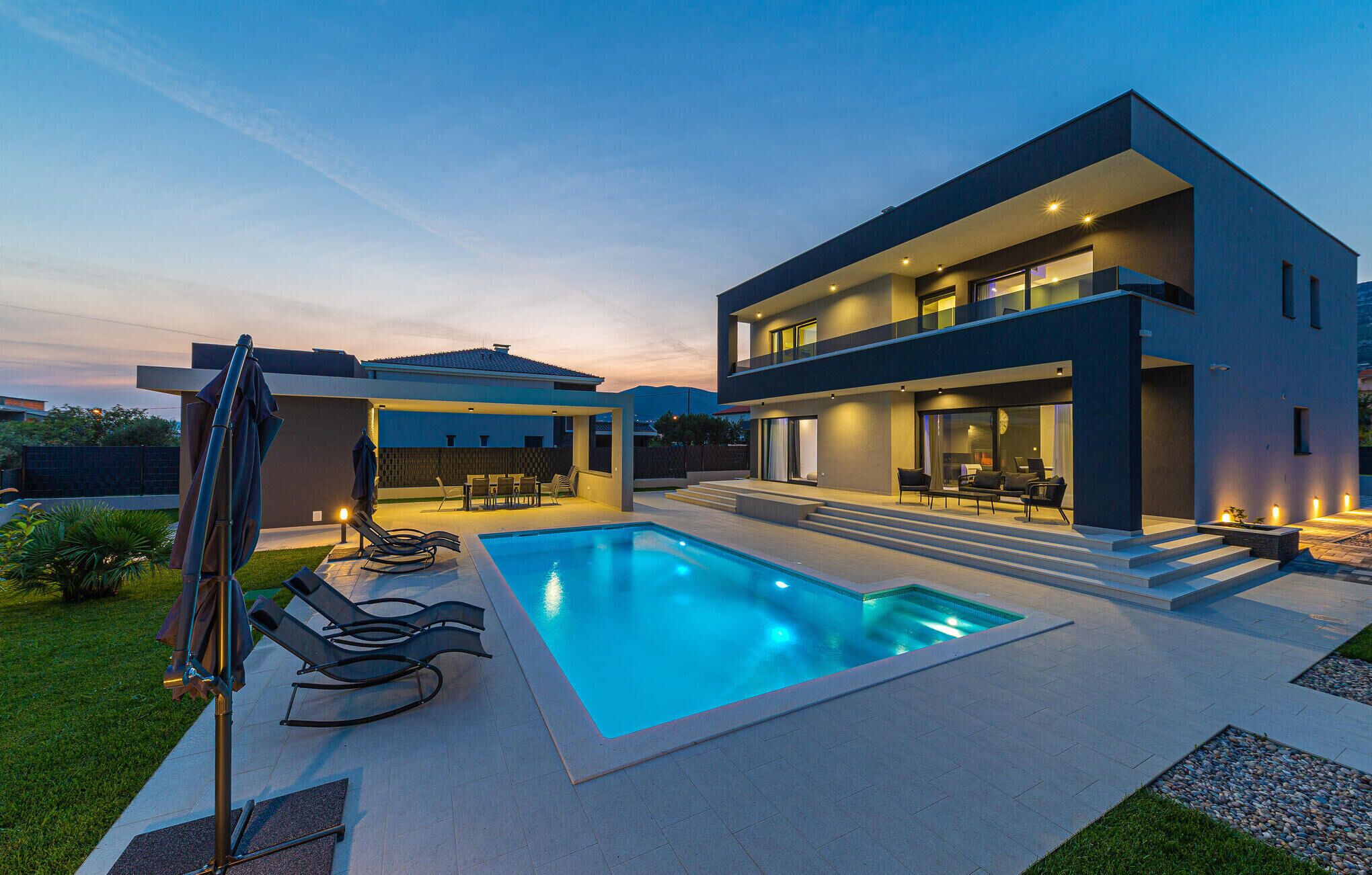 A modern two-story house with a swimming pool, outdoor seating, and a covered patio area.