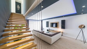 Un intérieur moderne avec un escalier, un espace de vie comprenant un canapé, un téléviseur et une lampe sur pied.