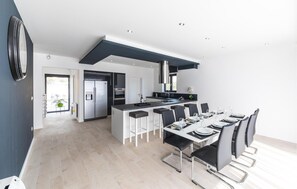 Een moderne keuken met een centraal eiland, roestvrijstalen apparatuur en een eetgedeelte met een lange tafel en stoelen.