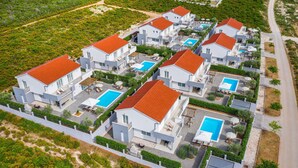 Un complejo residencial moderno con varias casas, cada una con piscina y zonas de estar al aire libre.