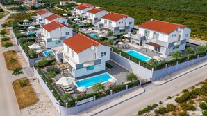 Un moderno complejo residencial con varias casas de dos pisos, una piscina central y un jardín bien cuidado.