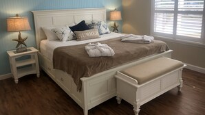 Un dormitorio con cama, mesitas de noche, un banco y una ventana con persianas.