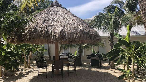 Un patio con sombrilla de paja, una parrilla y asientos.