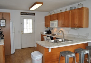 A kitchen with wooden cabinets, a white refrigerator, a microwave, a sink, and a trash can.