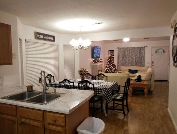A kitchen with a double sink, dining table with chairs, a small trash bin, and a Christmas tree.