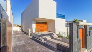 Un edificio moderno con tejado plano, puerta de madera y una escalera que conduce a la entrada.