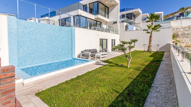 Una casa moderna de dos pisos con piscina, mobiliario exterior y un césped bien cuidado.