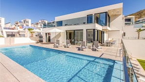 Un edificio moderno de dos pisos con piscina, mobiliario exterior y vistas despejadas del entorno.