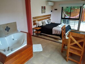 Un dormitorio con una bañera grande, una cama con colcha blanco y negro, una silla de madera y vistas a una hamaca en el exterior.