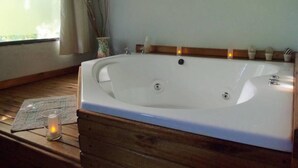 A large freestanding bathtub in a room with a wooden floor, a window with curtains, and a small candle on a placemat. - Ruca Lemu (Chascomus)