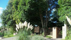 A gated entrance with a gravel path leading to a building, surrounded by lush greenery and tall grasses. - Ruca Lemu (Chascomus)