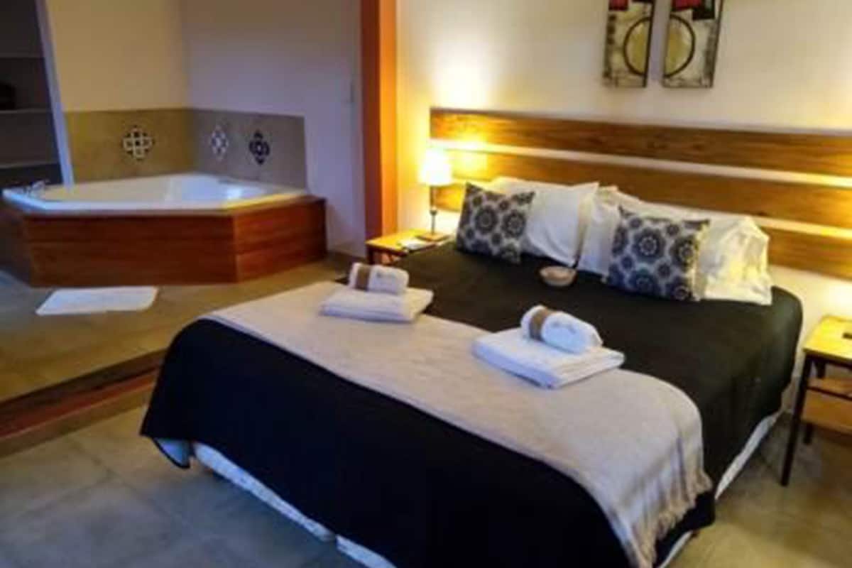 Habitación de hotel con una cama grande, una bañera independiente y una mesita de noche pequeña.