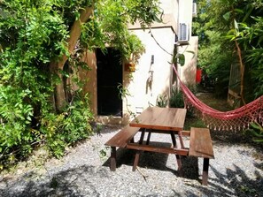 A wooden picnic table with benches, a hammock, and a building with a door and air conditioning unit.
