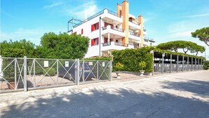 Ein mehrstöckiges Wohngebäude mit Balkonen, einem umzäunten Parkplatz und umgebender Bepflanzung.