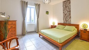 Ein Schlafzimmer mit einem hölzernen Bett, einem Nachttisch mit Lampe, einer Kommode und einem Fenster mit Vorhängen.