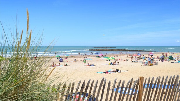 Ein Strand mit Menschen, die sich sonnen und schwimmen, Holzzaun und klarer Himmel.