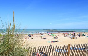 Ein Strand mit Menschen, die sich sonnen und schwimmen, Holzzaun und klarer Himmel.